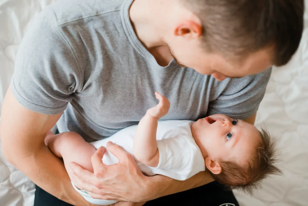 Padre sostiene a un bebé que está boca arriba mirándolo con cara de sorpresa